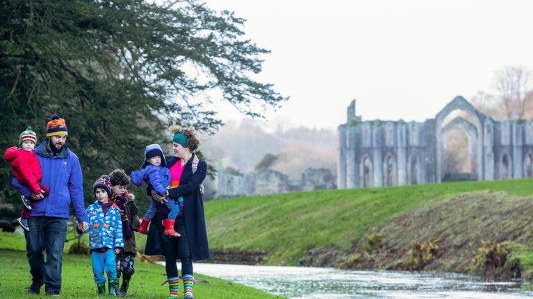 Family dressed for winter with a ruined arch and river of Fountains Abbey in the background